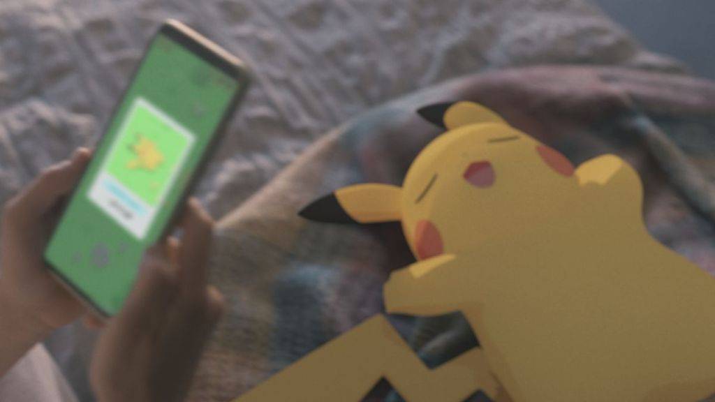 An image of a sleepy Pikachu, with a person holding up a phone using the Pokemon Sleep app